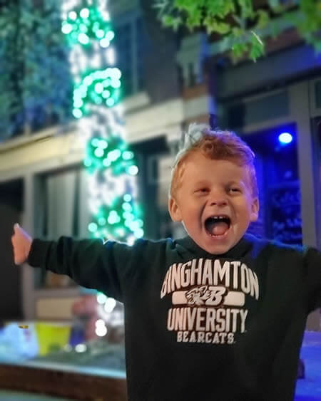 Cute child having fun in front of tree wrapped in green and white lights.